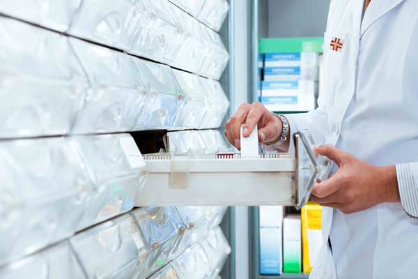 Doctor in a lab coat getting medicine out of a pharmacy shelf