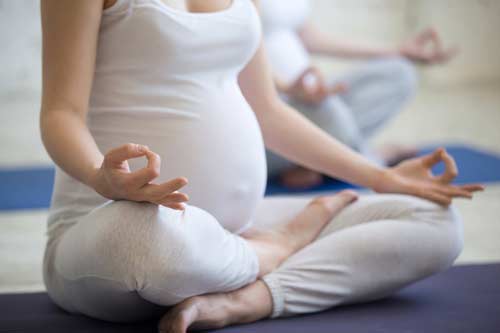 Pregnant woman wearing white meditating on a yoga mat